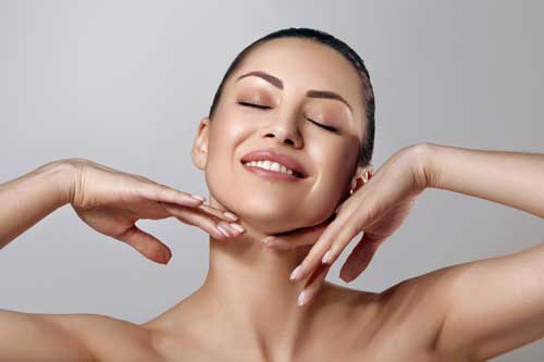Smiling woman touching face with closed eyes.